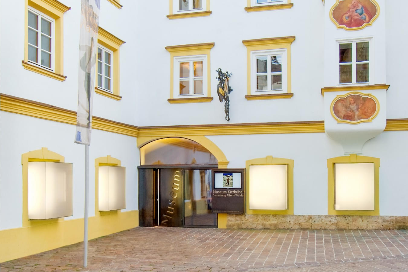 Hausfassade des Museum Kitzbühel im Stadtzentrum mit gelben Fensterrahmen und dem Eingangstor in der Hinterstadt Kitzbühel. 