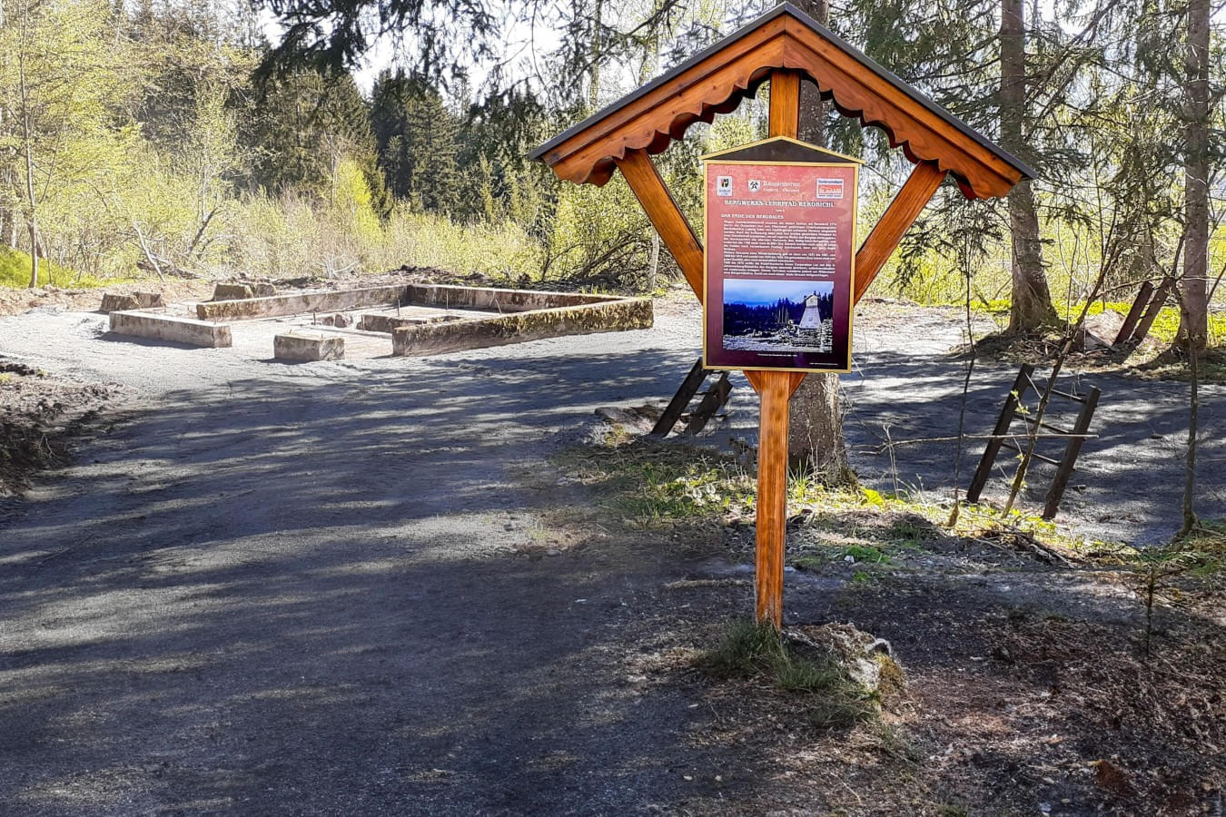 Infotafel des Bergwerks-Lehrpfads Reboichl vor den Grundmauern eines historischen Bergwerksgebäudes in einem Waldgebiet. 