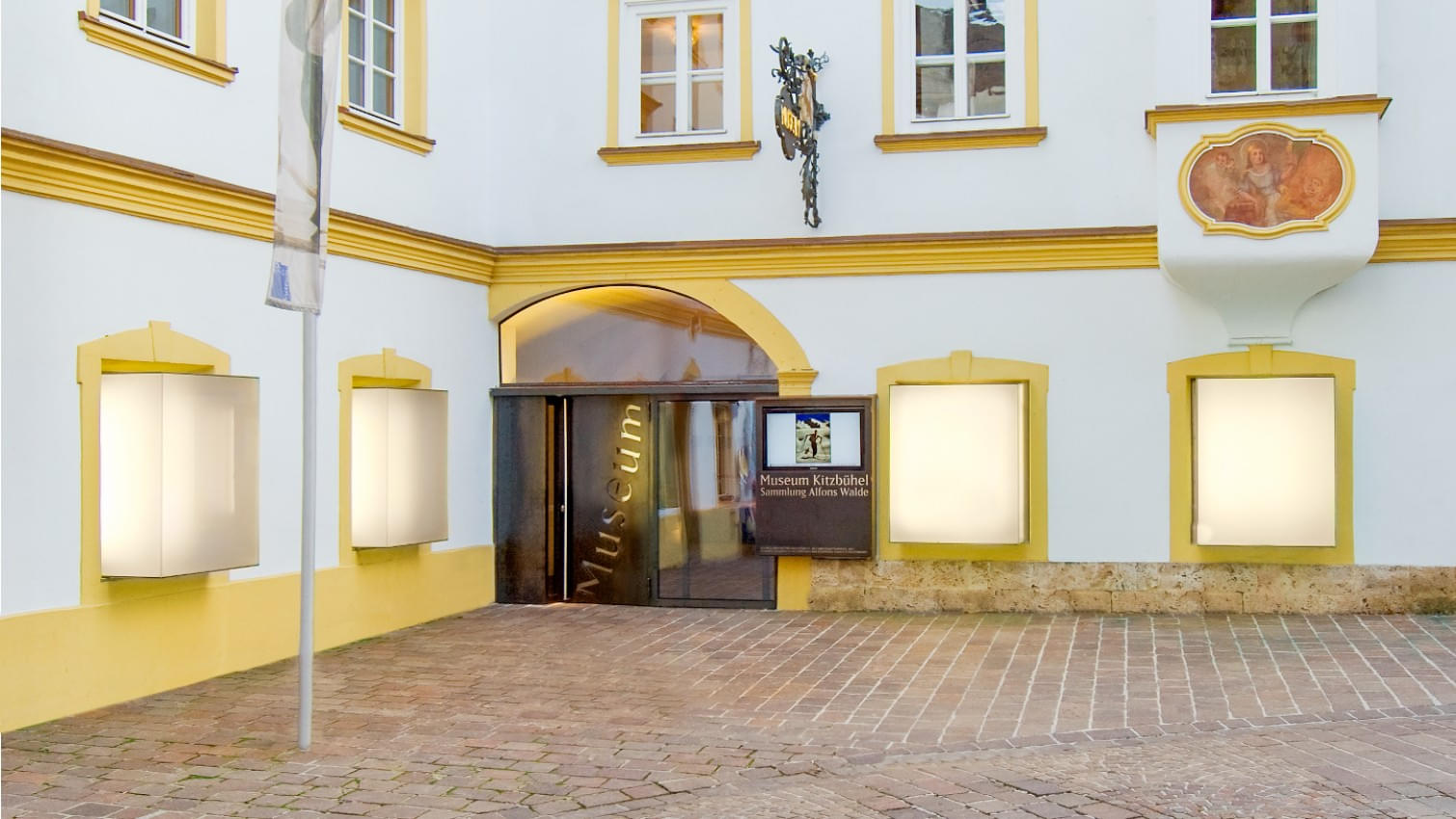 Eingangsbereich des Museum Kitzbühel im Stadtzentrum mit seiner weißen Fassade, gelben Fensterrahmen und dem Eingangstor. 