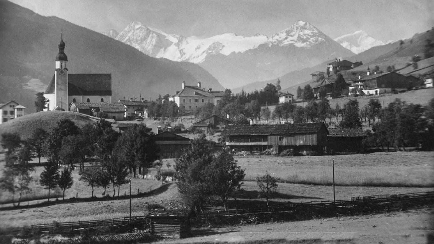 Historische Schwarz-Weiß-Aufnahme von Jochberg, mit Blick auf die Dorfkirche und den Großvenediger im Hintergrund.