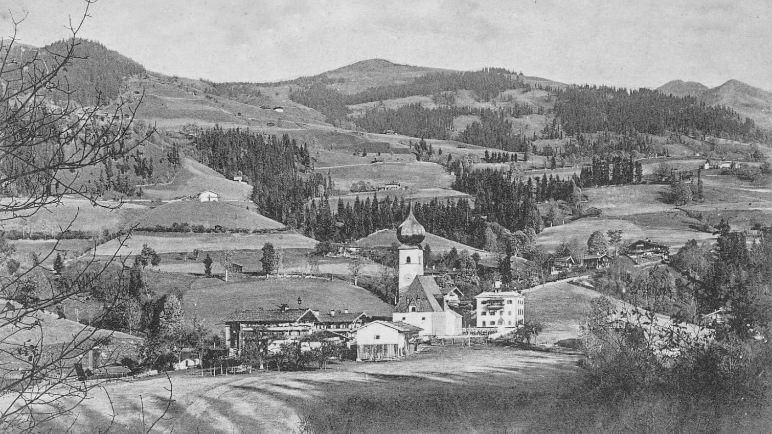 Historische Ansicht von Aurach in Tirol mit Kirche, umliegenden Gebäuden und hügeliger Landschaft. 